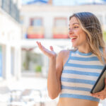 Young pretty woman holding a tablet at outdoors with surprise facial expression